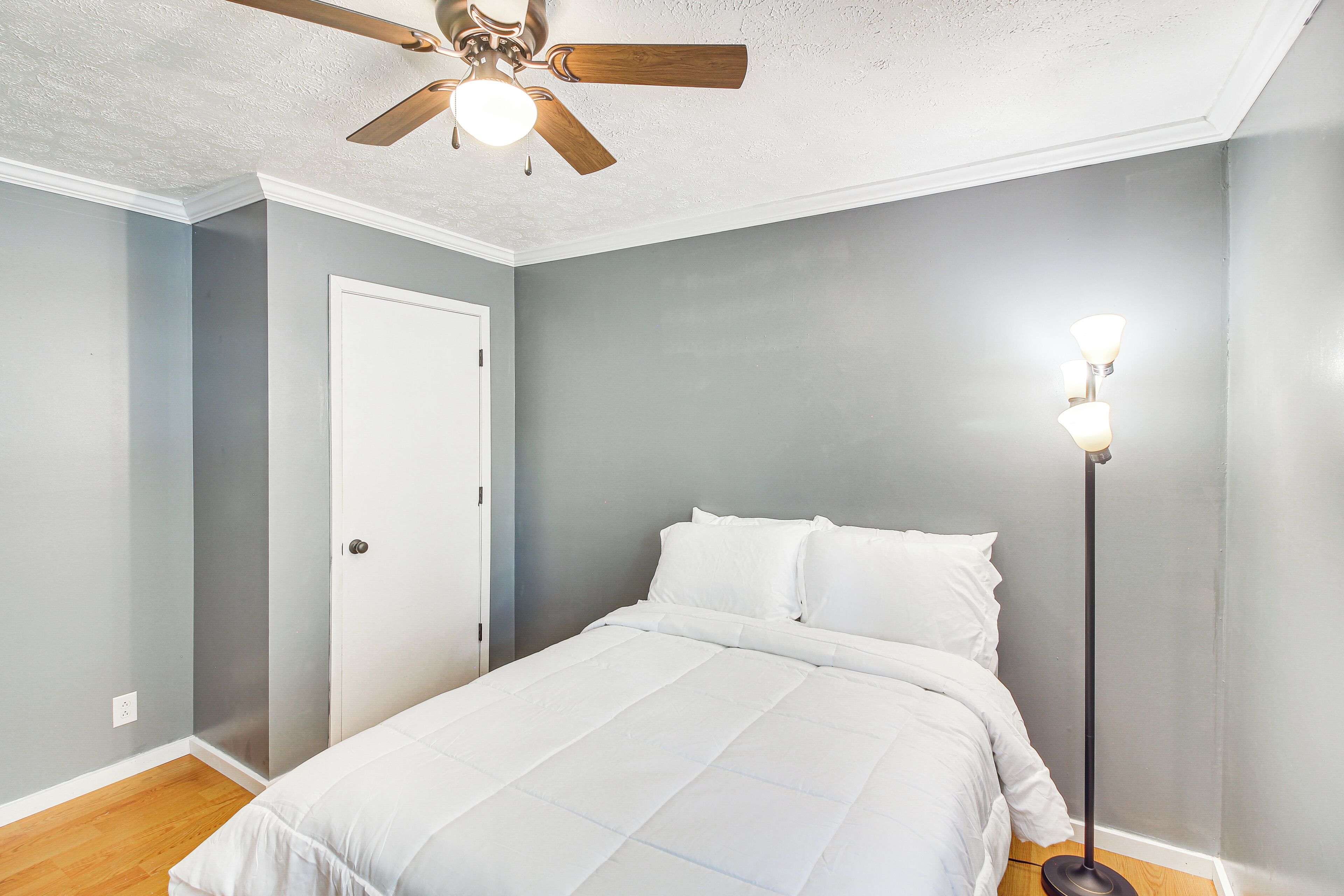 Een slaapkamer met een bed, een plafondventilator, een vloerlamp en een deur.