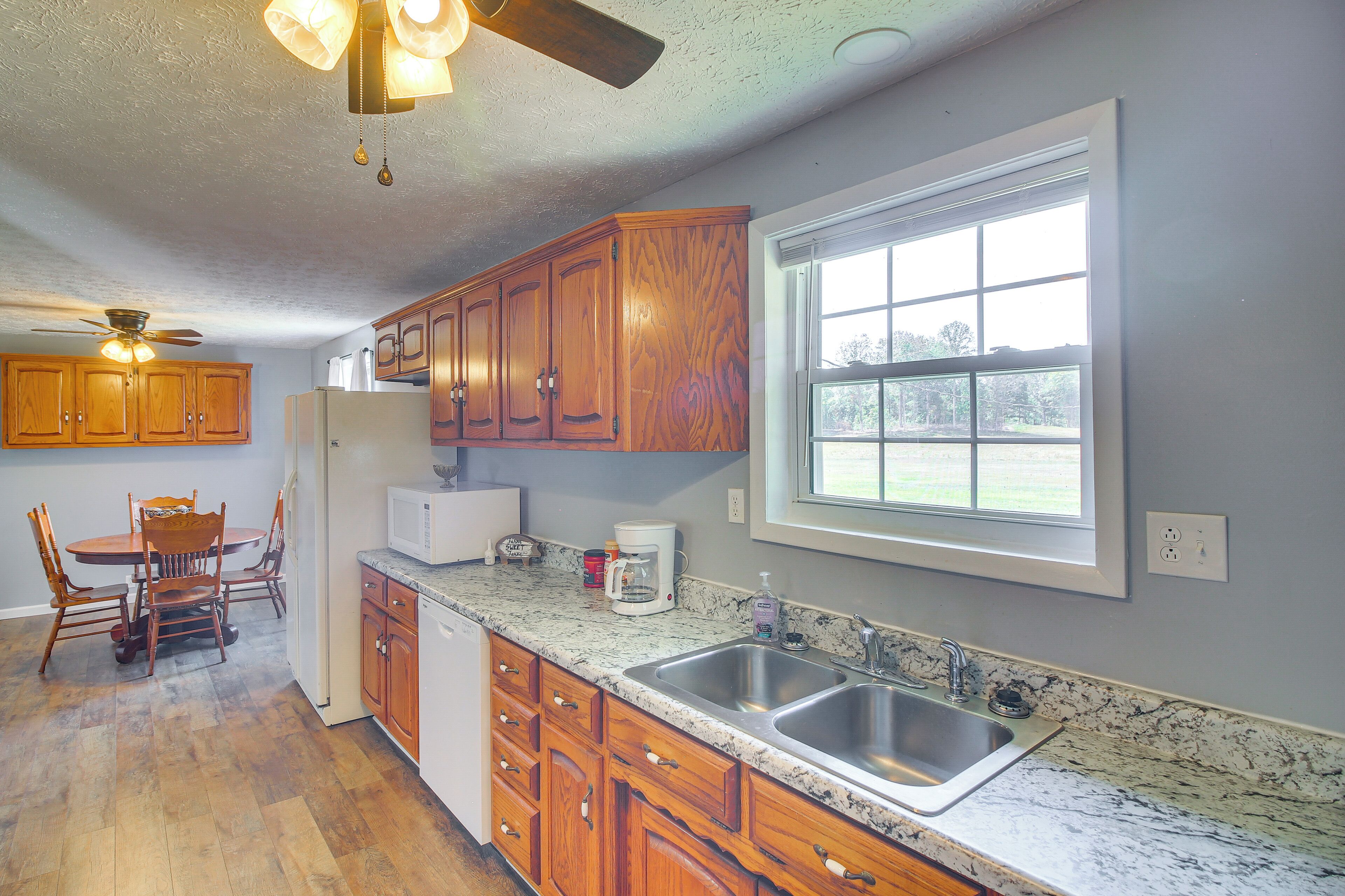 A kitchen with wooden cabinets, a granite countertop, a double sink, and a dining area with a table and chairs.
