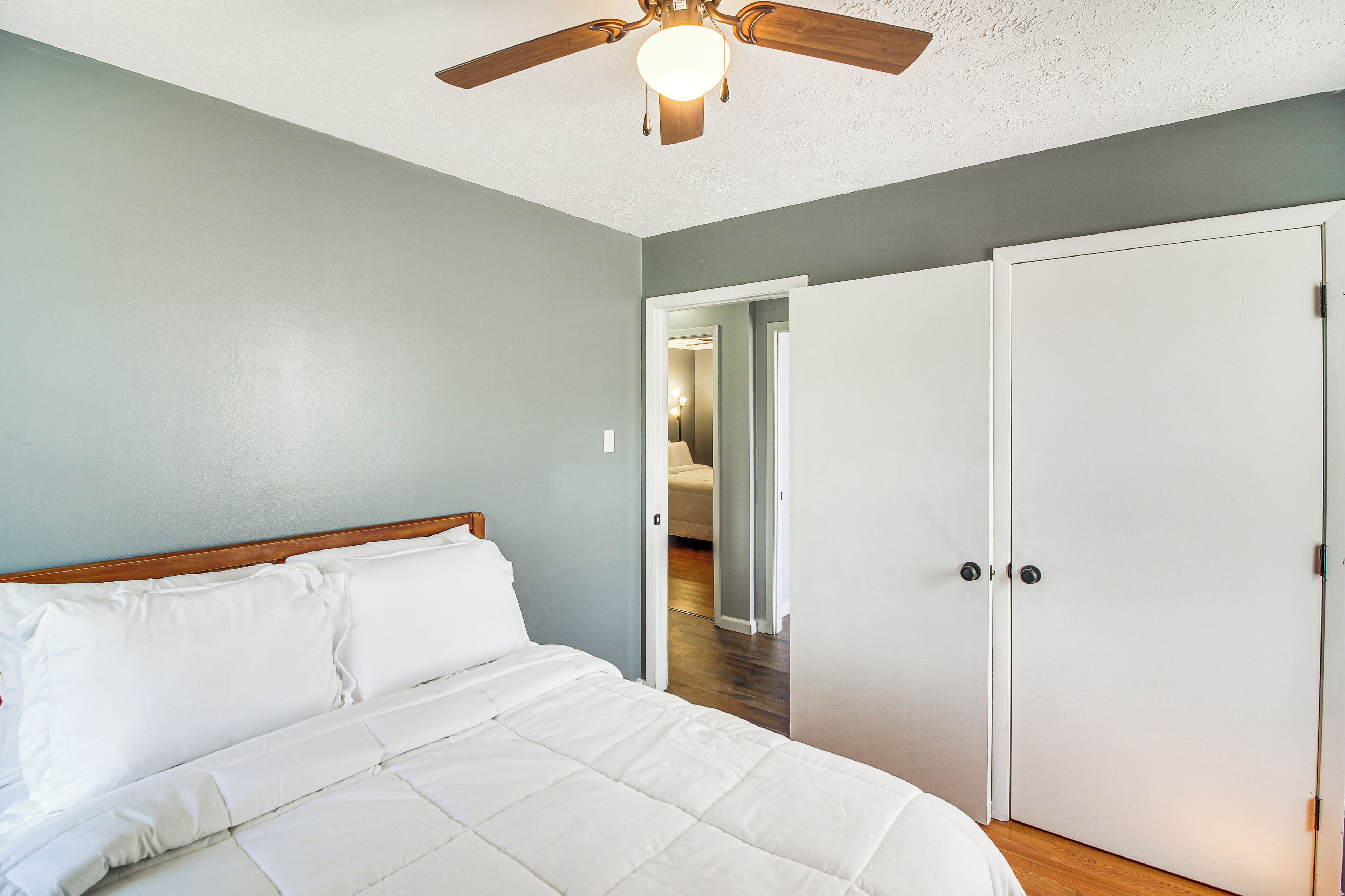 A bedroom with a bed, a ceiling fan, and a door leading to another room.