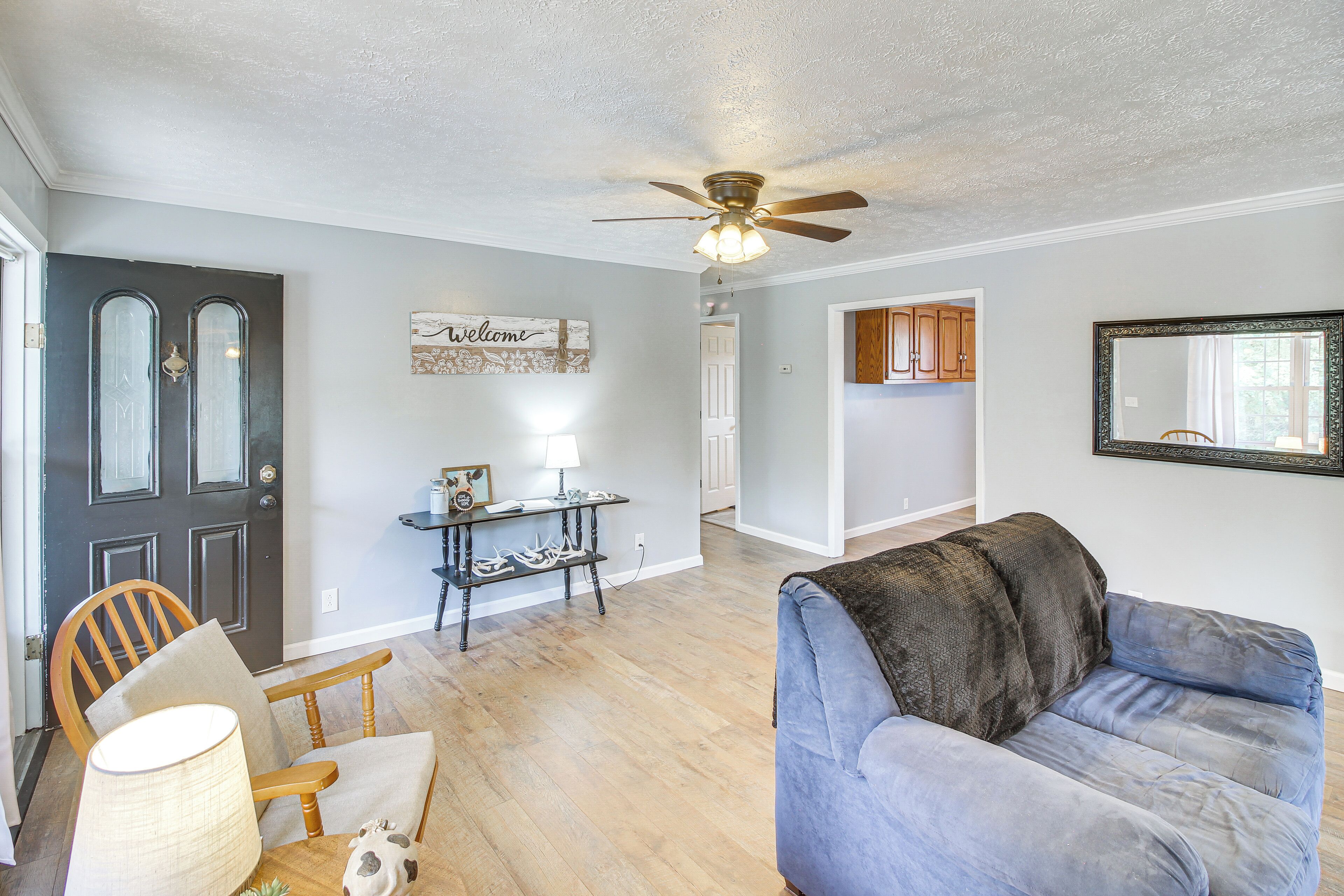 A living room with a ceiling fan, a dark door, a light table, and a blue couch.