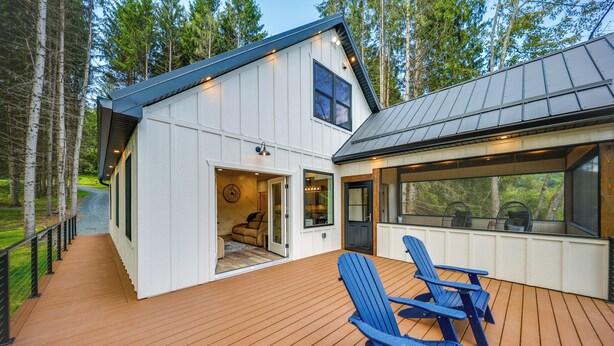 A modern house with a deck, two blue Adirondack chairs, and a large window overlooking the deck.