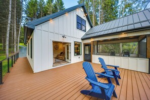 Une maison moderne dotée d’une terrasse, de deux chaises Adirondack bleues et d’une grande fenêtre donnant sur la terrasse.