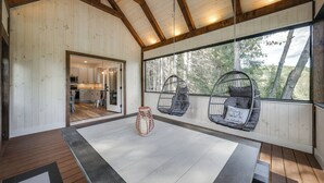 A spacious room with a large window, wooden ceiling beams, and a view of trees.