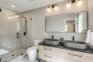 A modern bathroom with a glass-enclosed shower, two sinks, a large mirror, and a toilet.