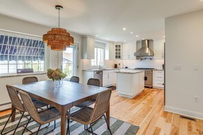 A modern kitchen with white cabinetry, a central island, and a dining area with wicker chairs. - Walk to Beach! Point Pleasant Home w/ Heated Pool (Point Pleasant Beach)