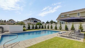 Une piscine rectangulaire avec un escalier en métal, entourée d’une pelouse verdoyante et d’une clôture blanche.