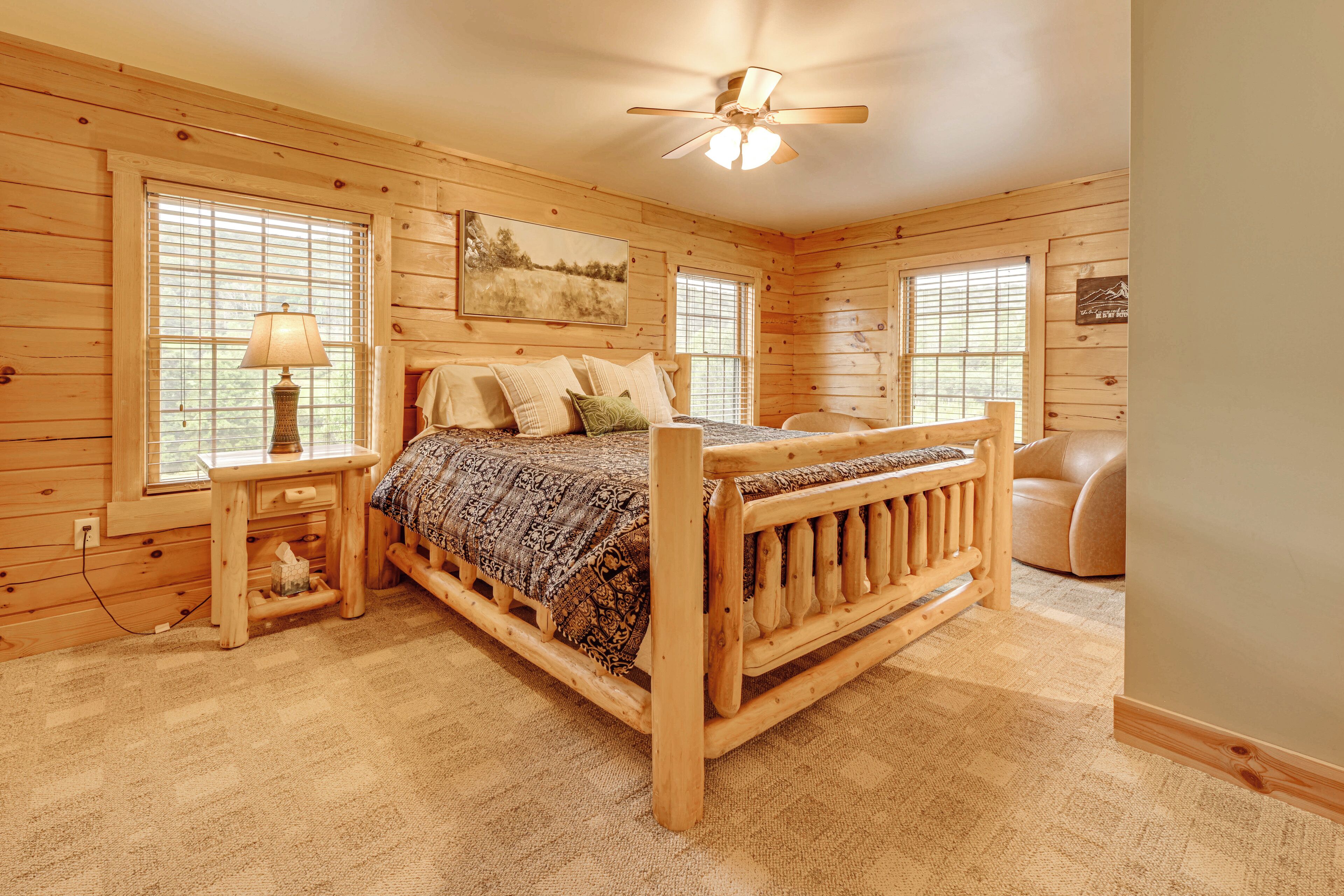 A wooden cabin bedroom with a bed, nightstands, a chair, and a ceiling fan.