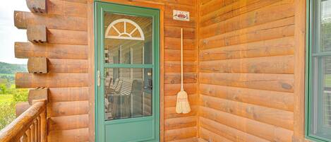 A wooden cabin with a green door, a broom hanging on the wall, and a doormat on the porch.