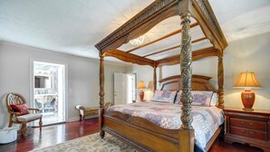 A four-poster bed with a floral-patterned bedspread, a wooden nightstand with a vase, and a chair with a cushion. - Near Lake Erie, Harbor & Parks: Conneaut Getaway! (Conneaut)