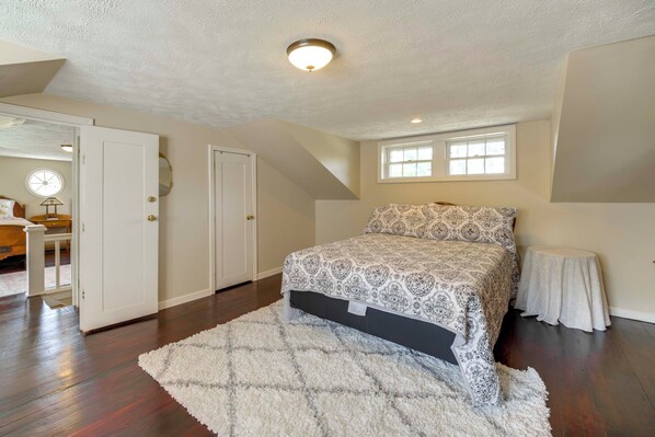 A bedroom with a large bed, a white rug, a window, and a door leading to another room.