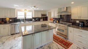 A spacious kitchen with white cabinetry, a large island with a black countertop, stainless steel appliances, and a red patterned rug. - Near Lake Erie, Harbor & Parks: Conneaut Getaway! (Conneaut)