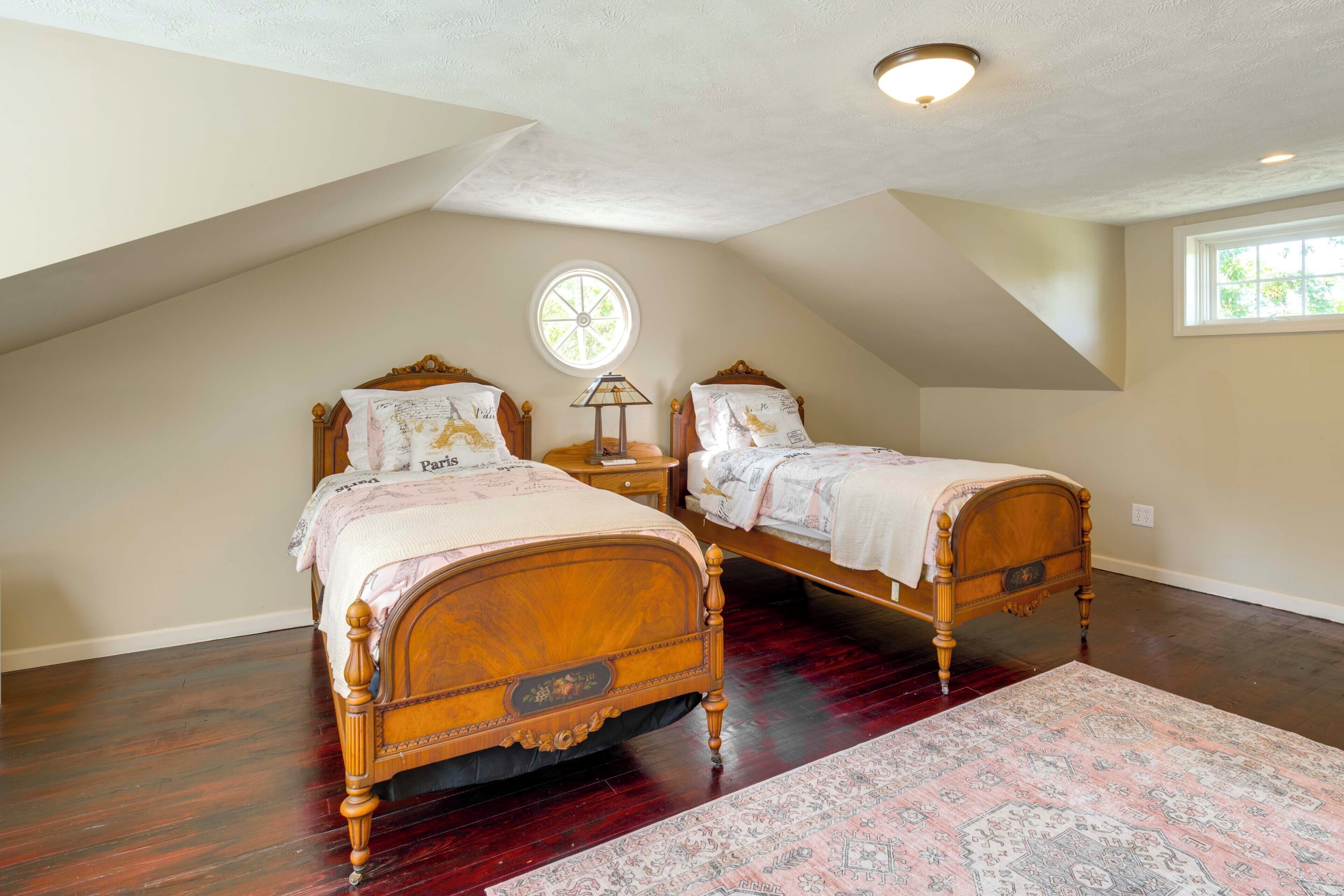 A bedroom with two wooden beds, a large window, a ceiling fan, and a patterned rug.
