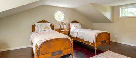A bedroom with two wooden beds, a large window, a ceiling fan, and a patterned rug.