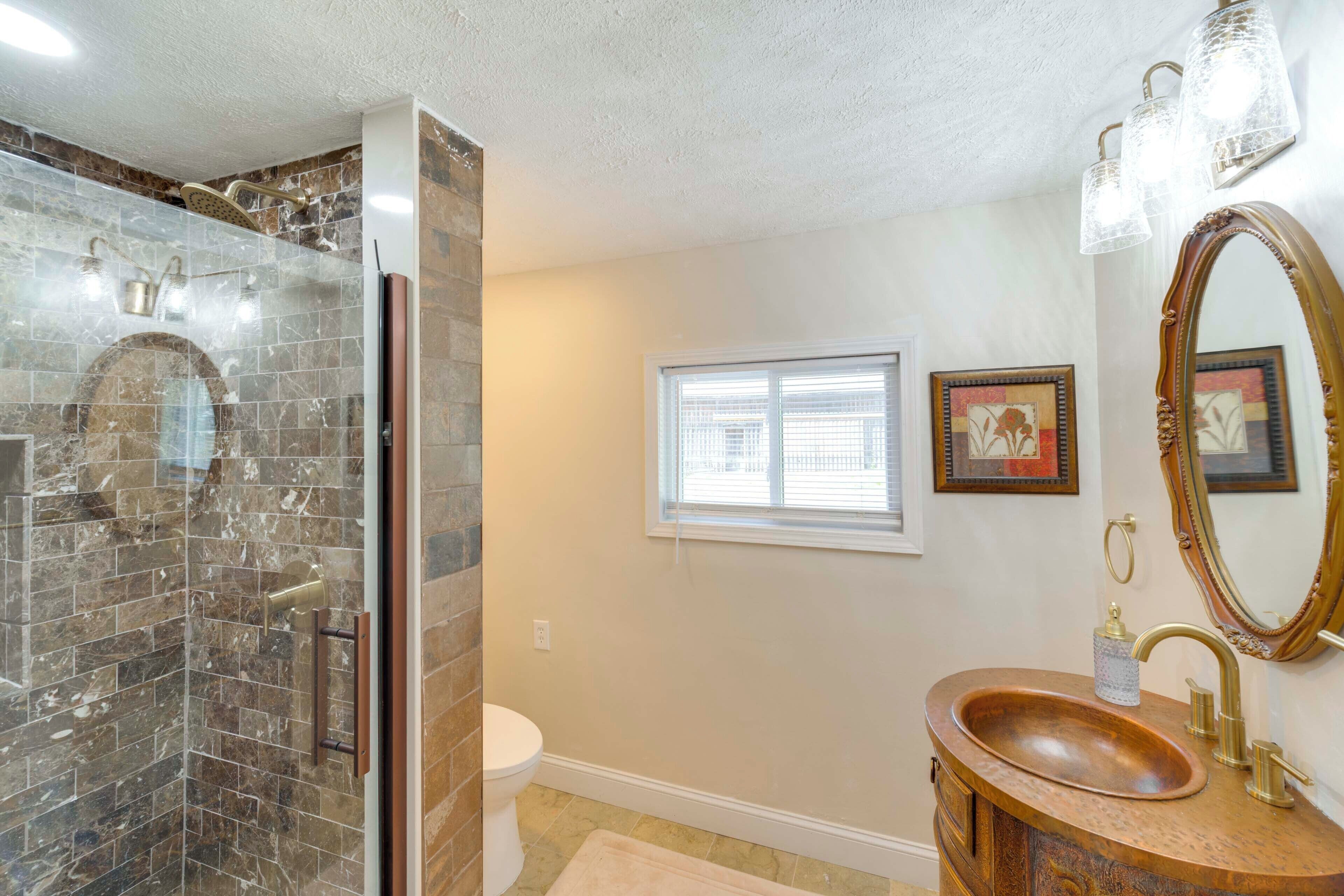A bathroom with a glass-enclosed shower, a freestanding toilet, a vanity with a wooden basin, and a large mirror.
