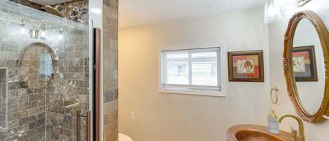 A bathroom with a glass-enclosed shower, a freestanding toilet, a vanity with a wooden basin, and a large mirror.