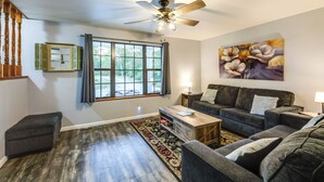 A living room with a ceiling fan, a large window with curtains, a dark-colored sofa, a coffee table, and a rug. - Kentucky Countryside Escape: 5 Mi to Williamstown! (Williamstown)