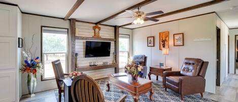 A living room with a TV, wooden furniture, a patterned rug, and a ceiling fan.