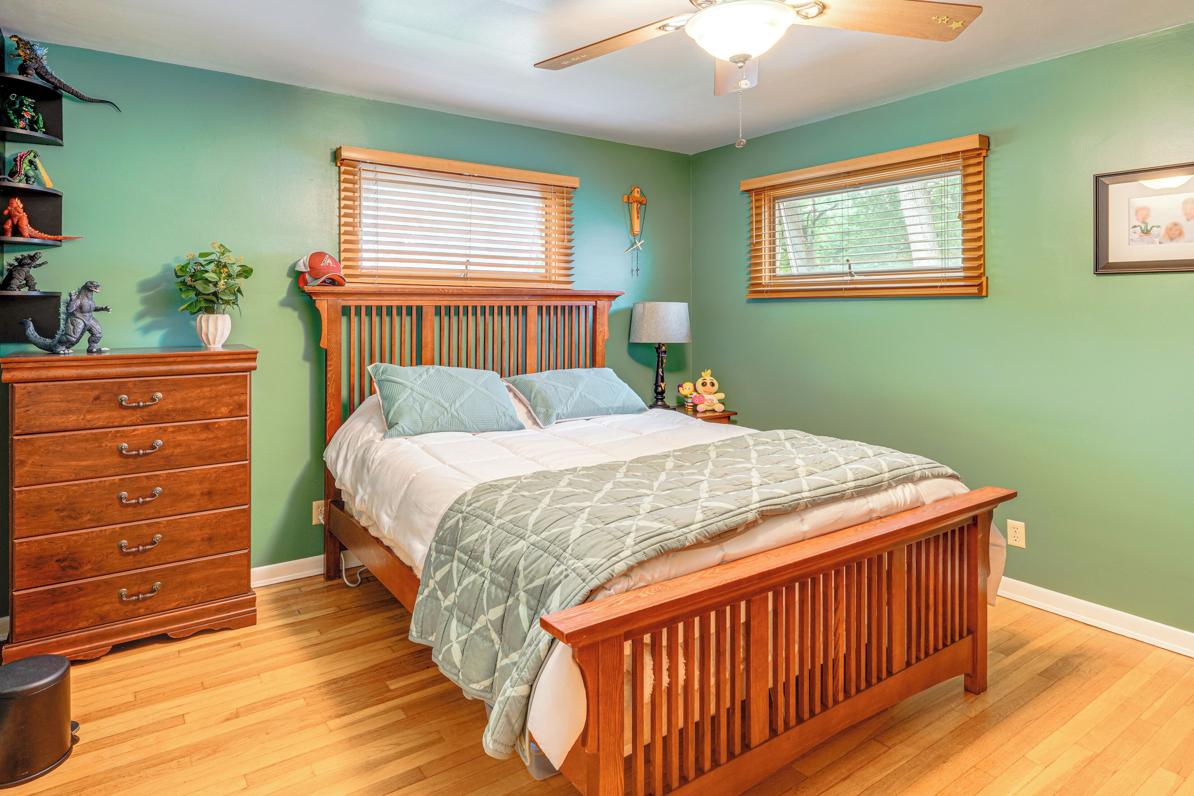 A bedroom with a wooden bed, a dresser, a ceiling fan, and a window with blinds.