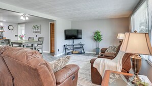 A living room with a brown leather sofa, a coffee table, a TV, and a dining area with a table and chairs. - Fish, Hike & Golf: Leisurely Navarre Home w/ Yard! (Navarre)