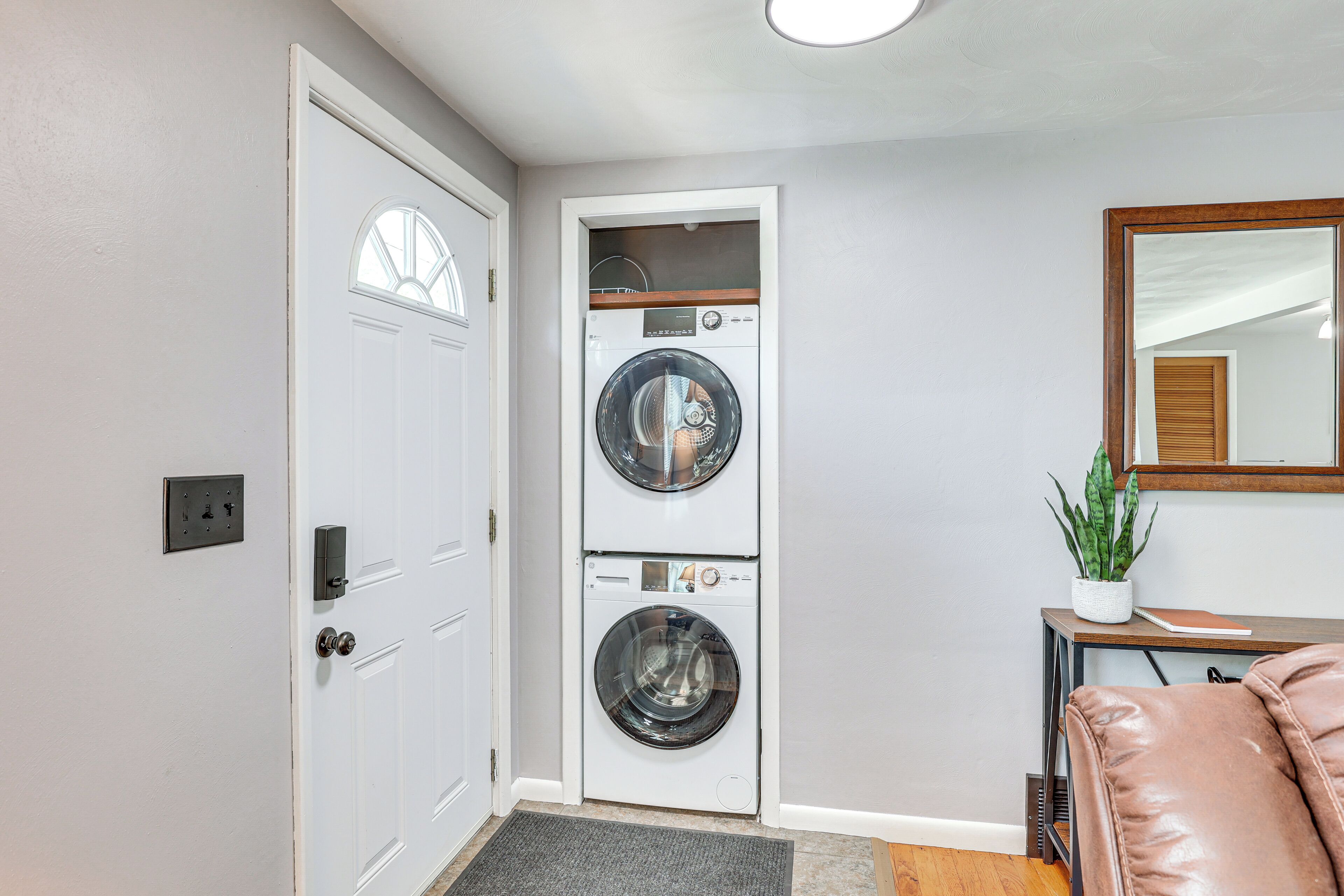 A laundry room with two stacked washing machines, a door with a keypad lock, a small potted plant, and a leather chair.