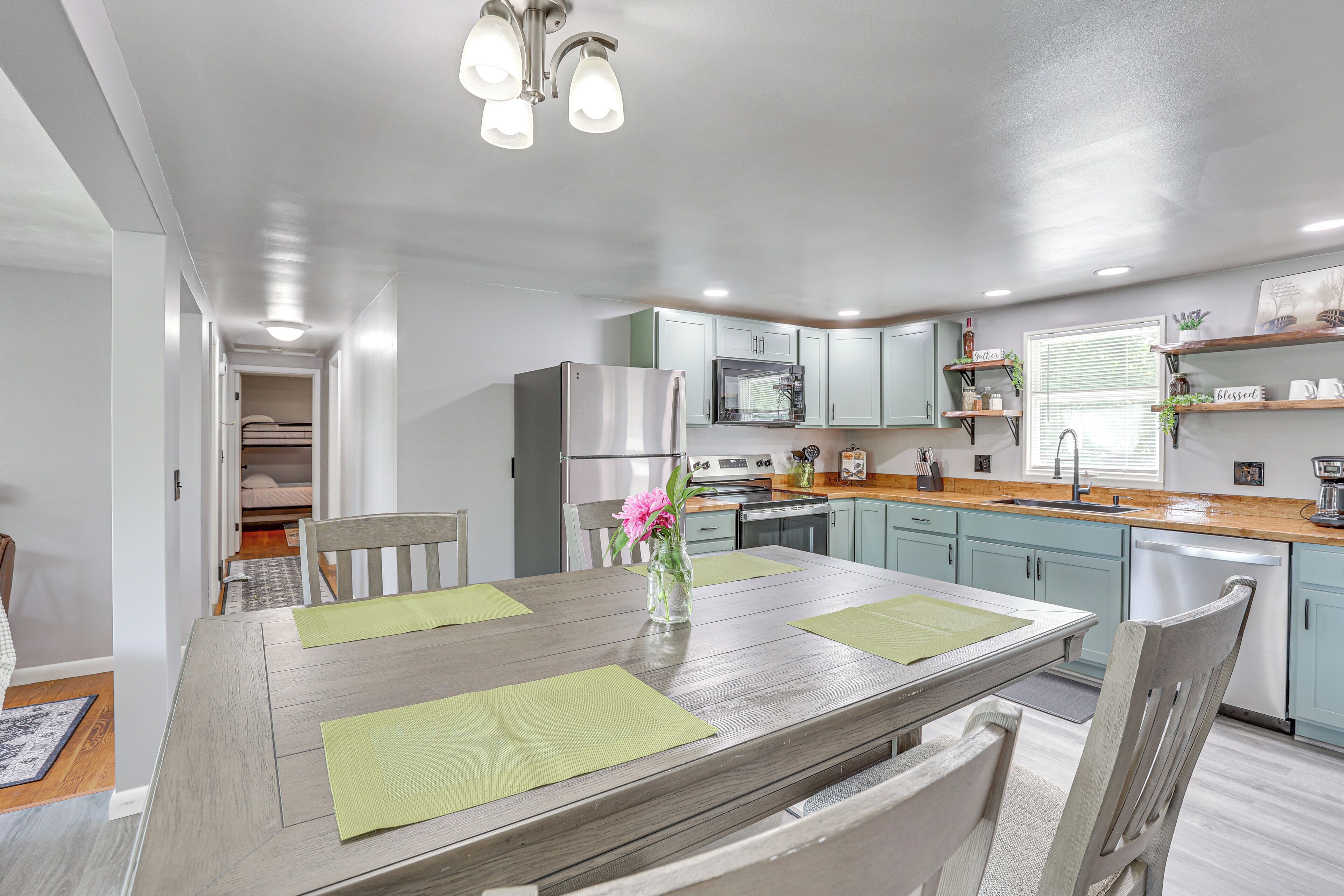 A modern kitchen with a central island, light blue cabinets, stainless steel appliances, and a window with blinds.