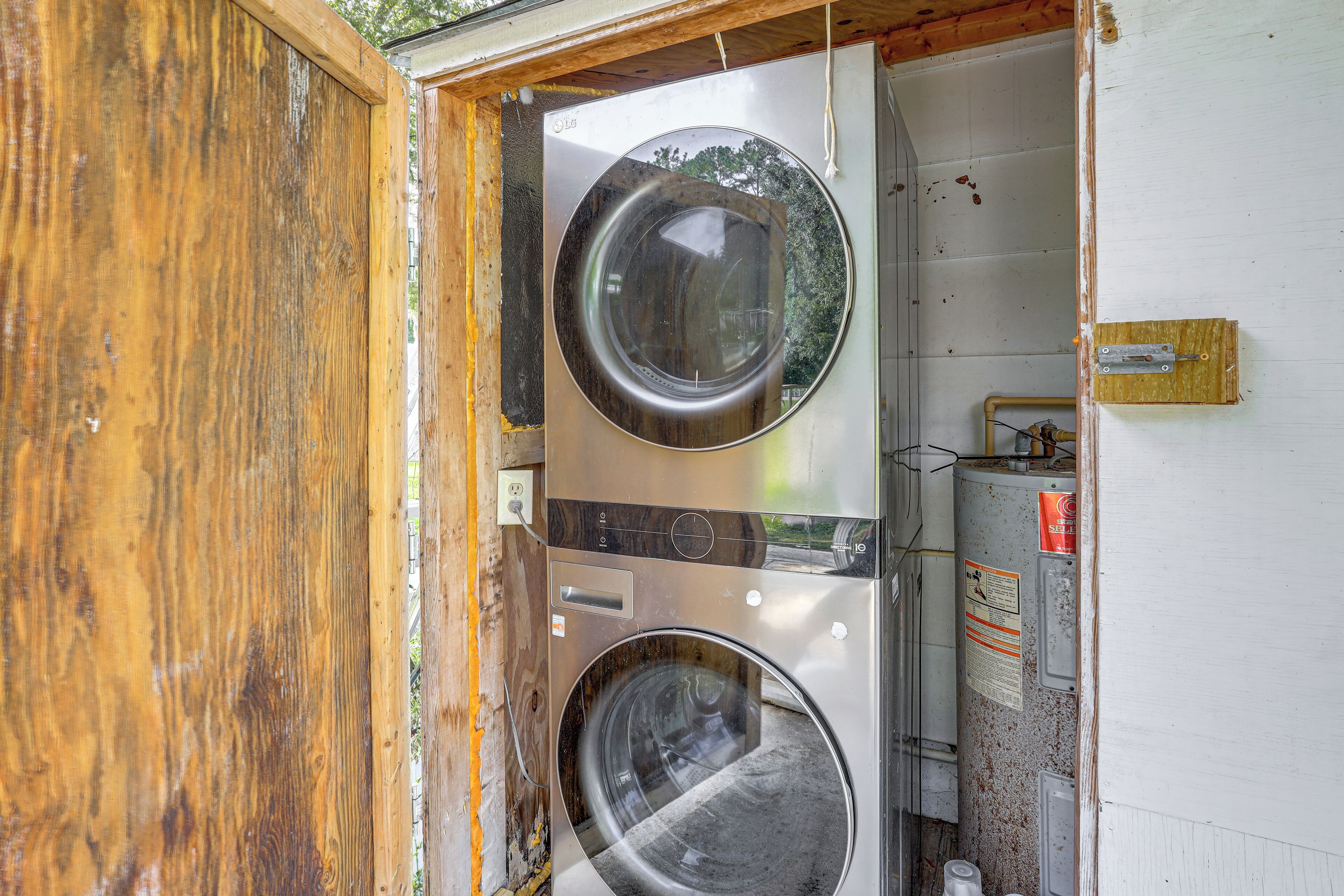 A room with two stacked washing machines, a wooden door, and a white wall with a safety sign.