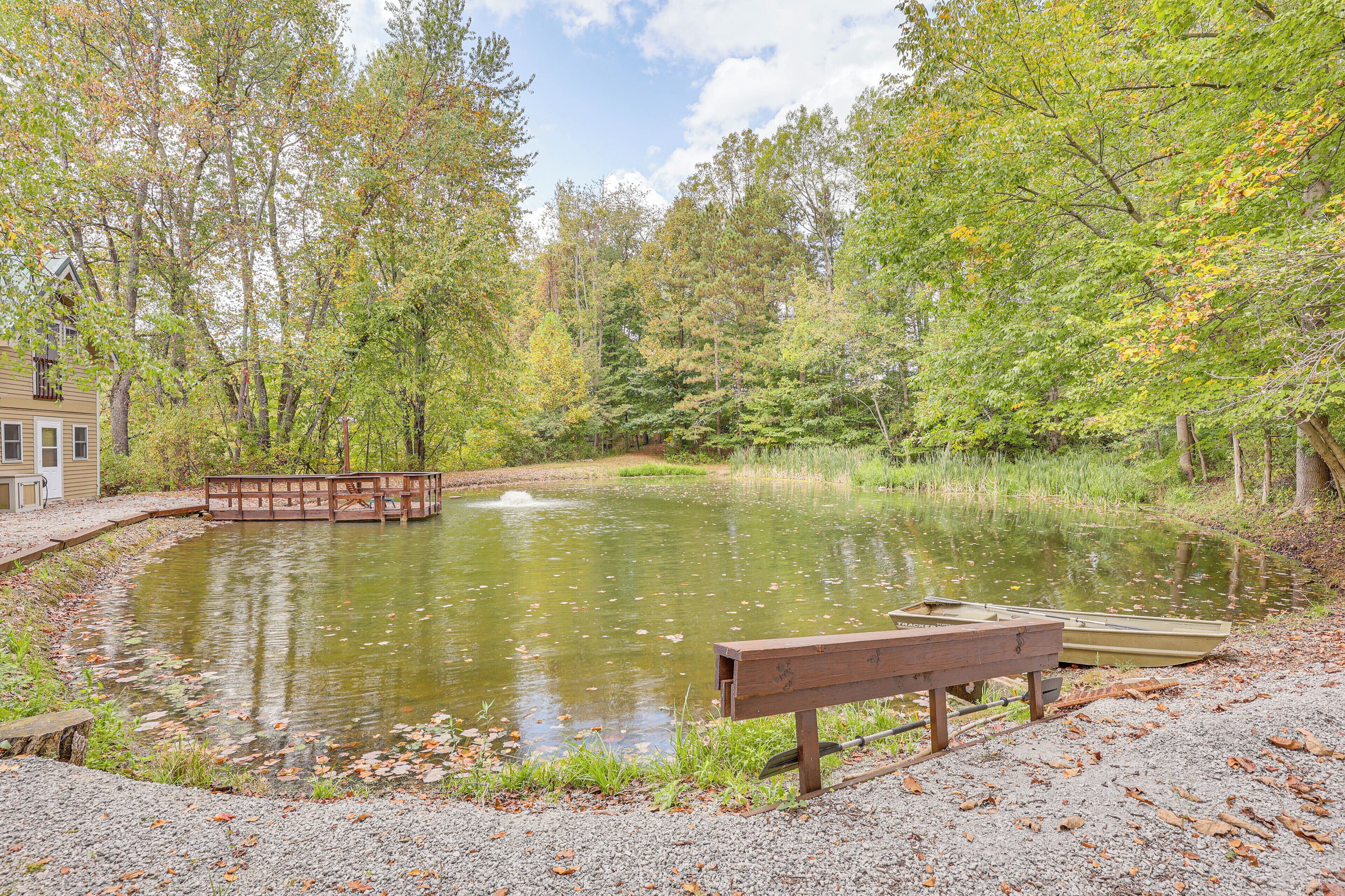 A serene pond with a wooden bench and a small boat, surrounded by trees and a wooden bridge.