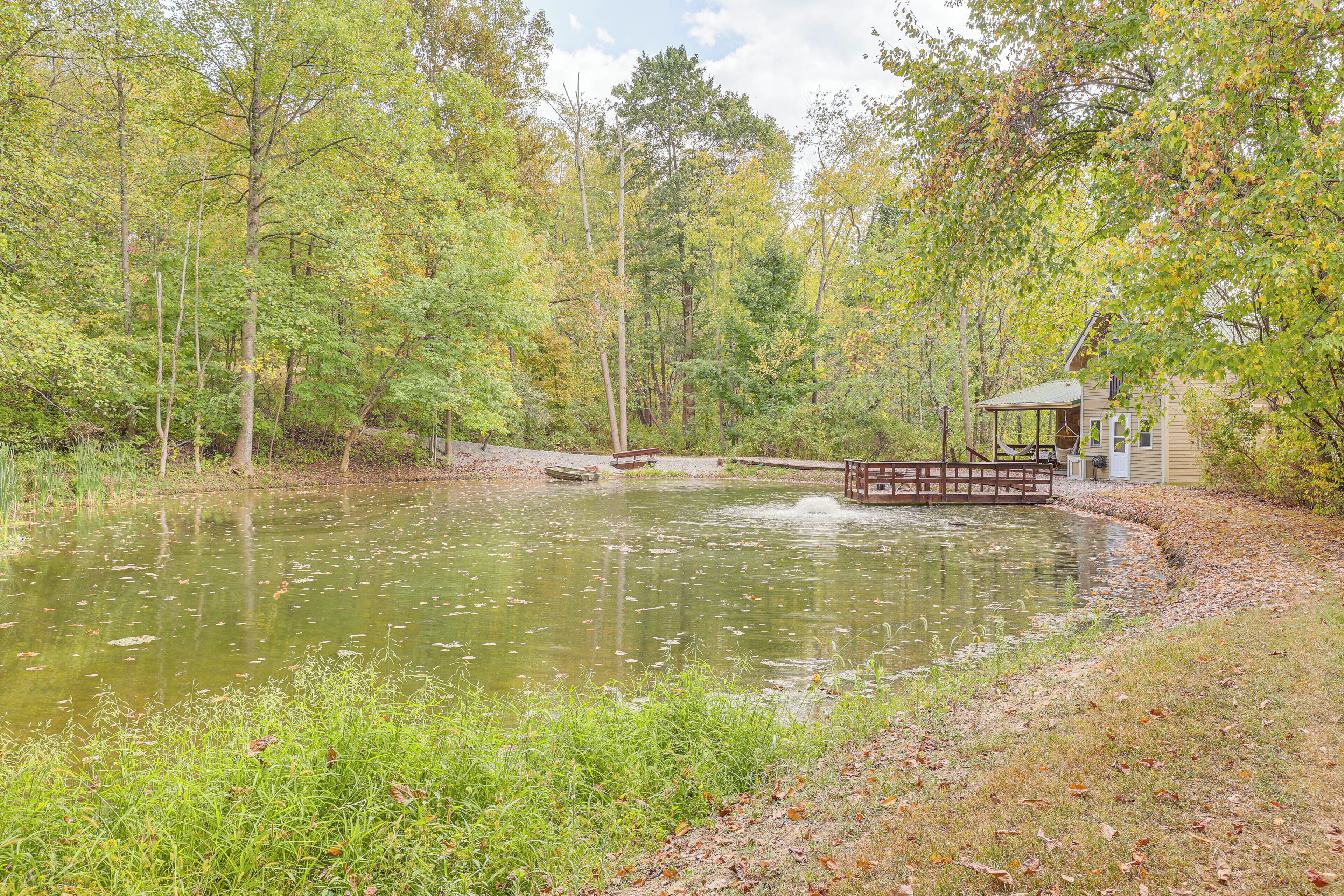 A pond surrounded by trees with a wooden bridge and a small building.