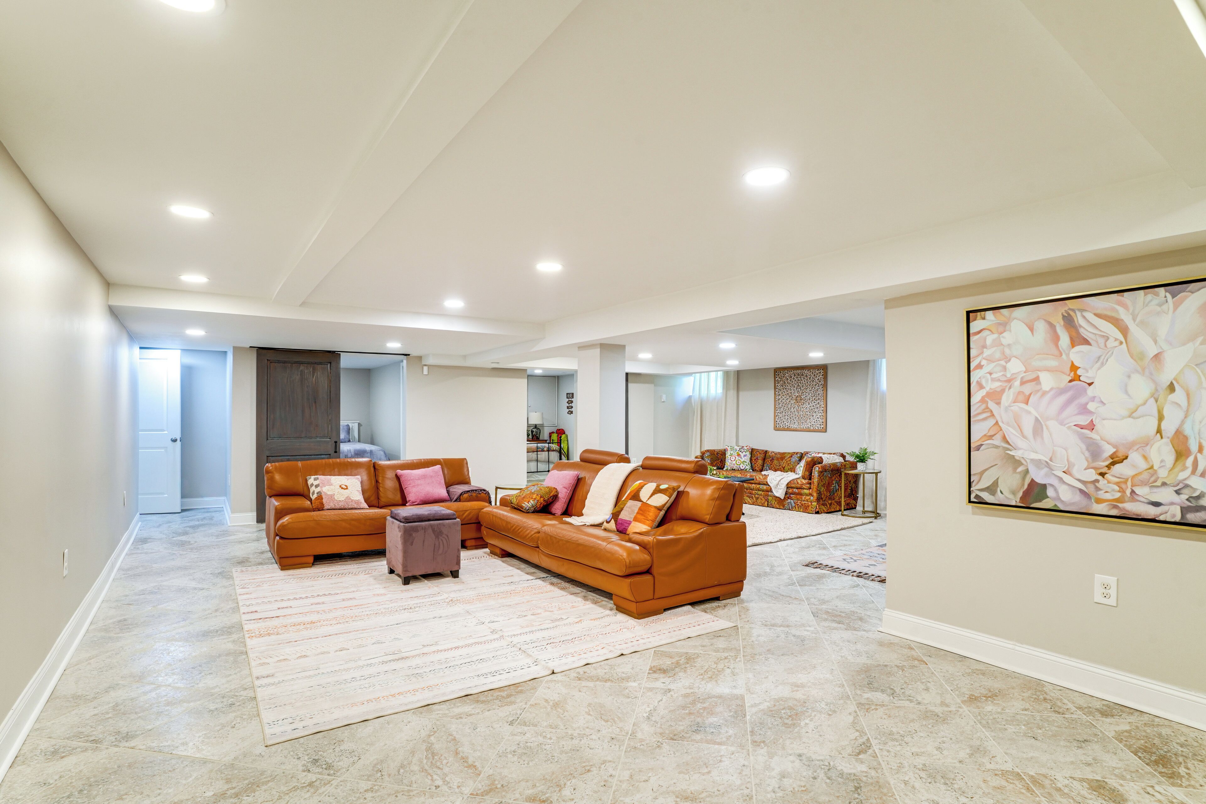 A spacious living room with a large brown leather sofa, a small ottoman, and a large painting on the wall.