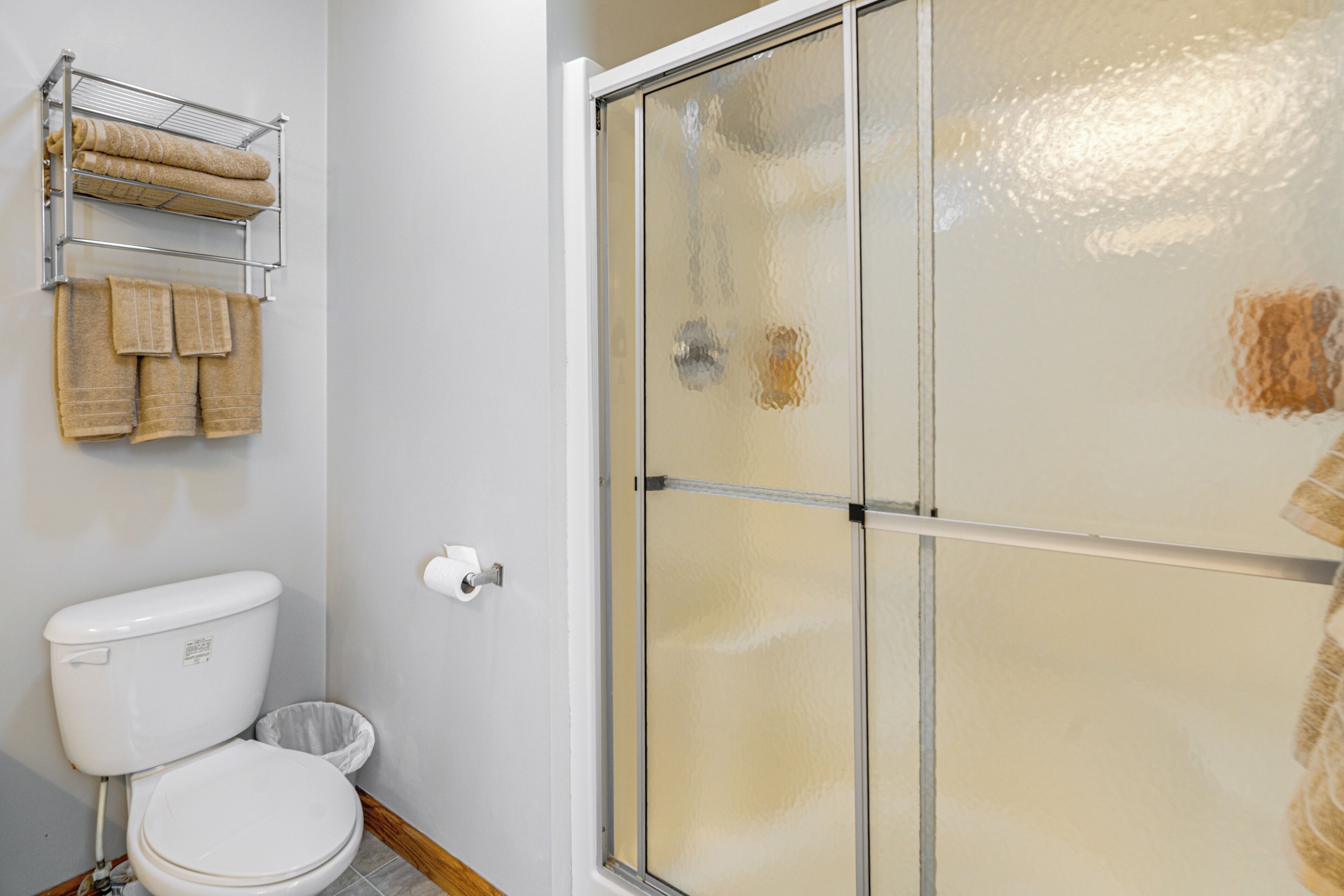 A bathroom with a toilet, a towel rack with towels, a glass shower enclosure, and a toilet paper holder.