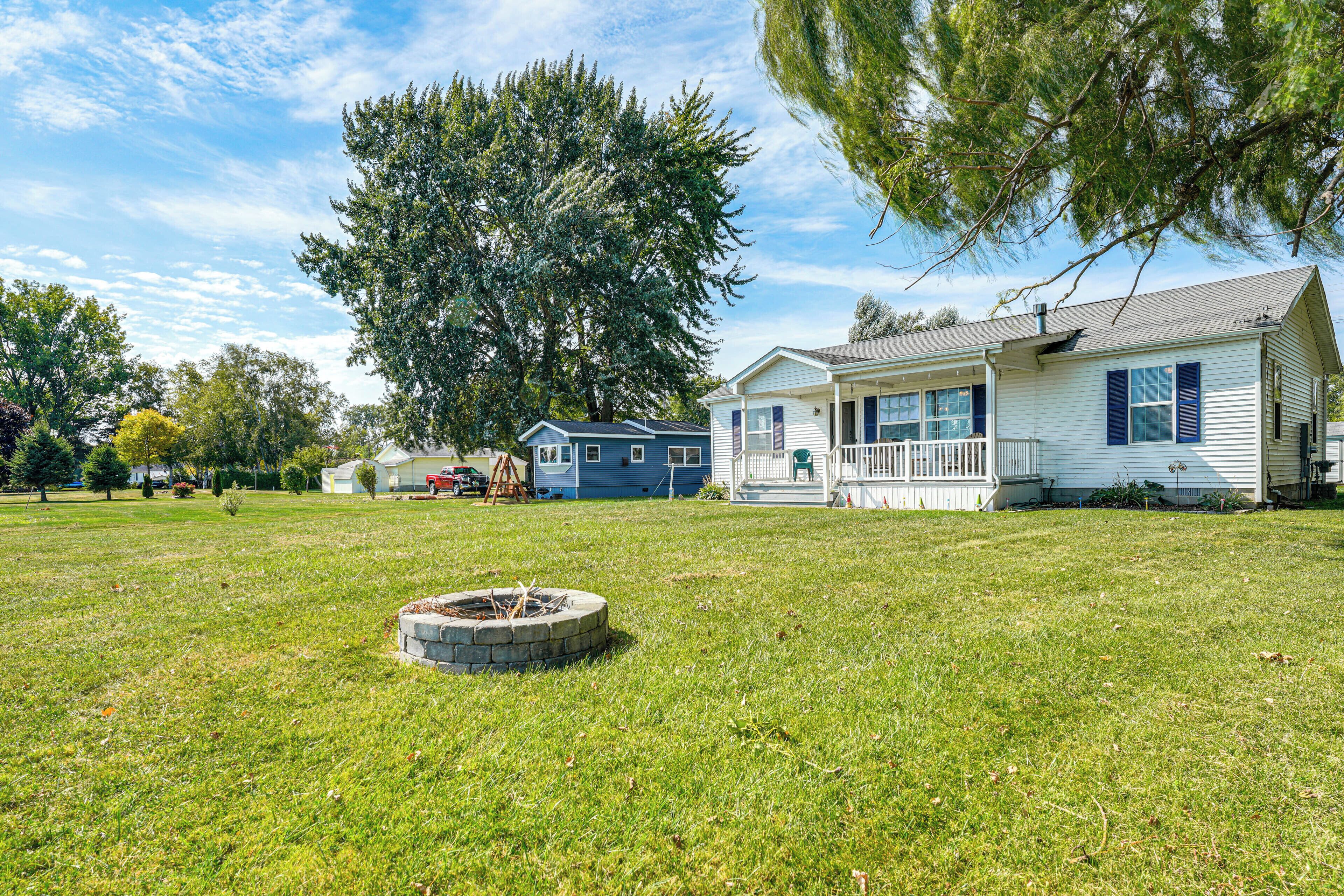 A house with a front porch, a fire pit in the yard, and a large tree in the background.