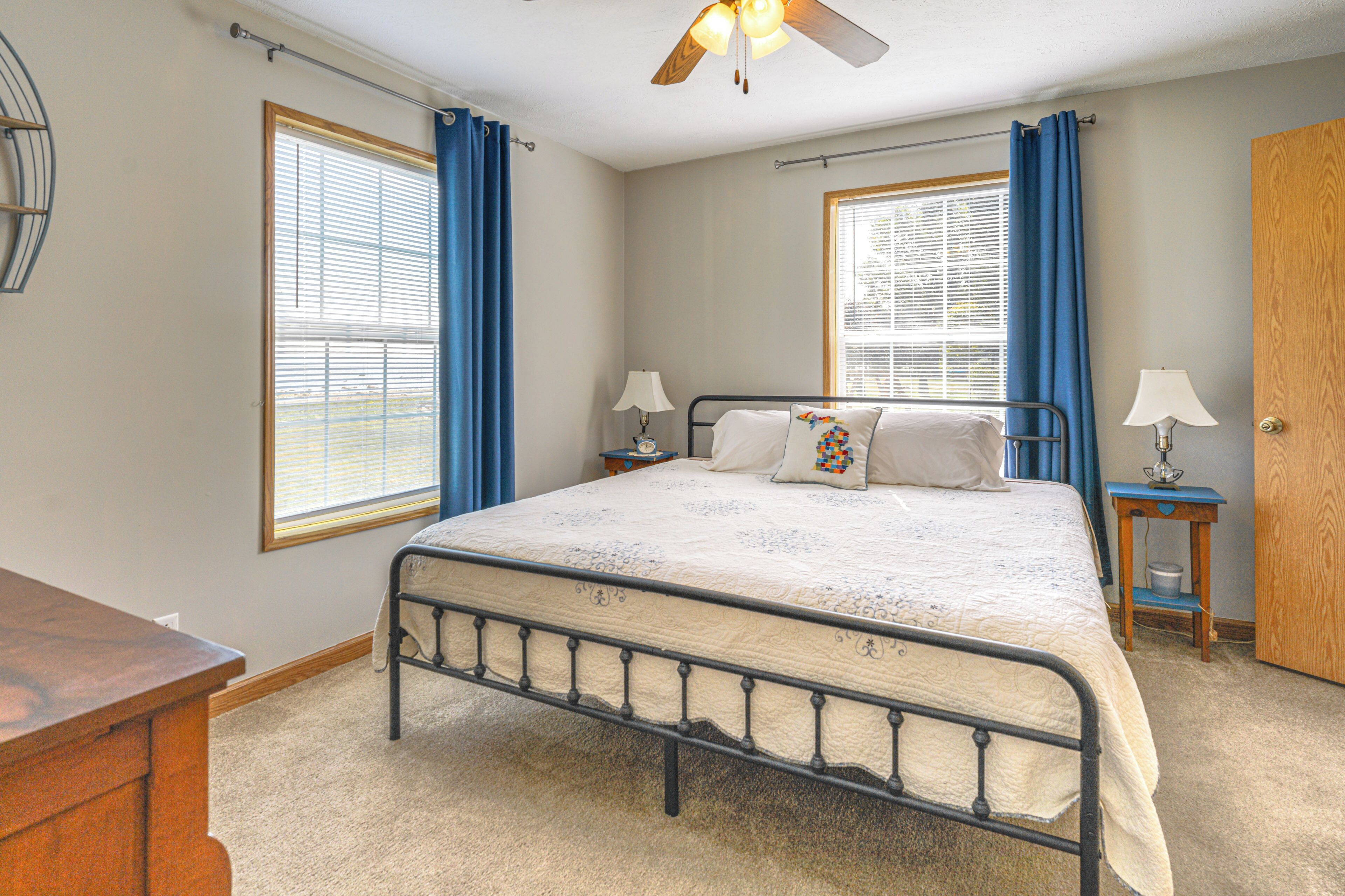 A bedroom with a bed, two bedside tables with lamps, a wooden door, and a ceiling fan.