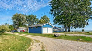A blue building with a garage, a dirt path, and a large tree. - Port Hope Escape: Fire Pit, Deck & Lake Views (Port Hope)