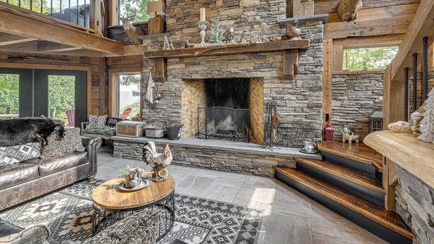 A rustic interior with a stone fireplace, leather furniture, and a wooden staircase. - Luxe Cabin Compound 4 Mi to Cameron State Forest! (Cameron)