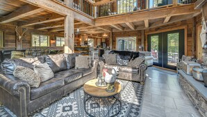 A spacious living room with a high ceiling, wooden beams, a fireplace, leather sofas, and a stone fireplace surround. - Luxe Cabin Compound 4 Mi to Cameron State Forest! (Cameron)