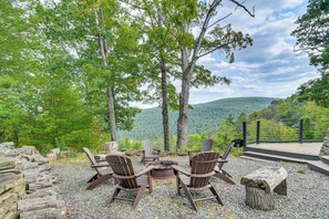 A deck with Adirondack chairs and a fire pit, overlooking a mountainous landscape.