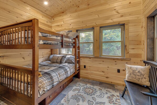 Un dormitorio de cabaña de madera con literas, un banco y una ventana que ofrece vistas a árboles.