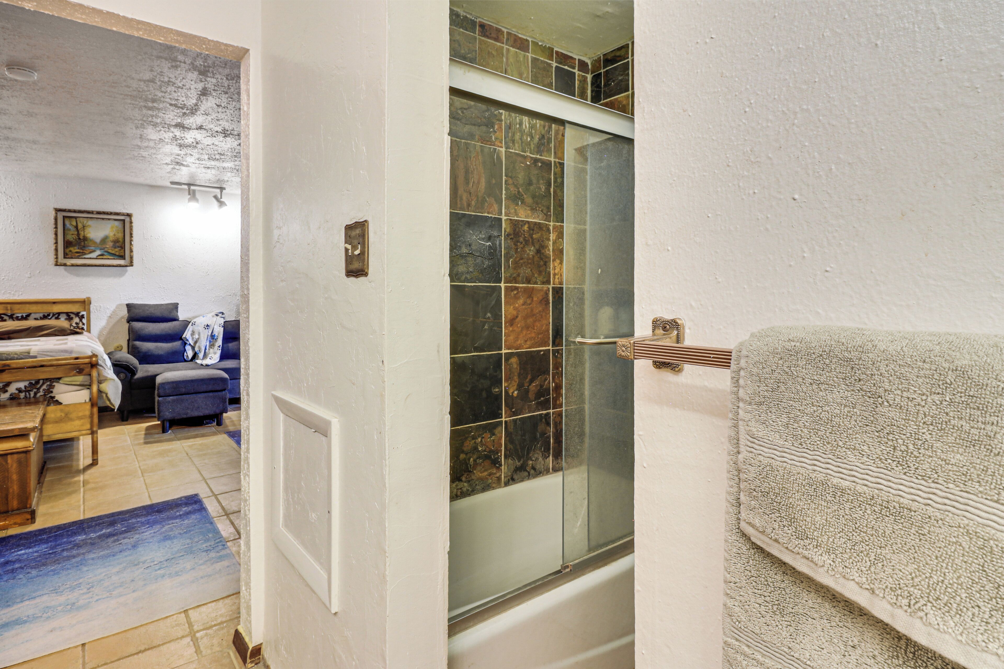 Un baño con bañera, cabina de ducha de vidrio, barra para toallas y un banco de madera.