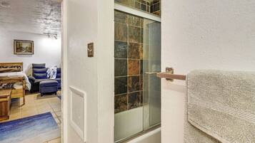 Un baño con bañera, cabina de ducha de vidrio, barra para toallas y un banco de madera.