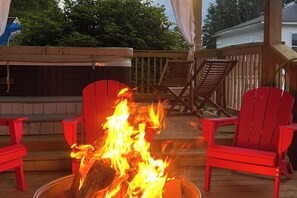 A deck with a fire pit in the center, surrounded by red Adirondack chairs.