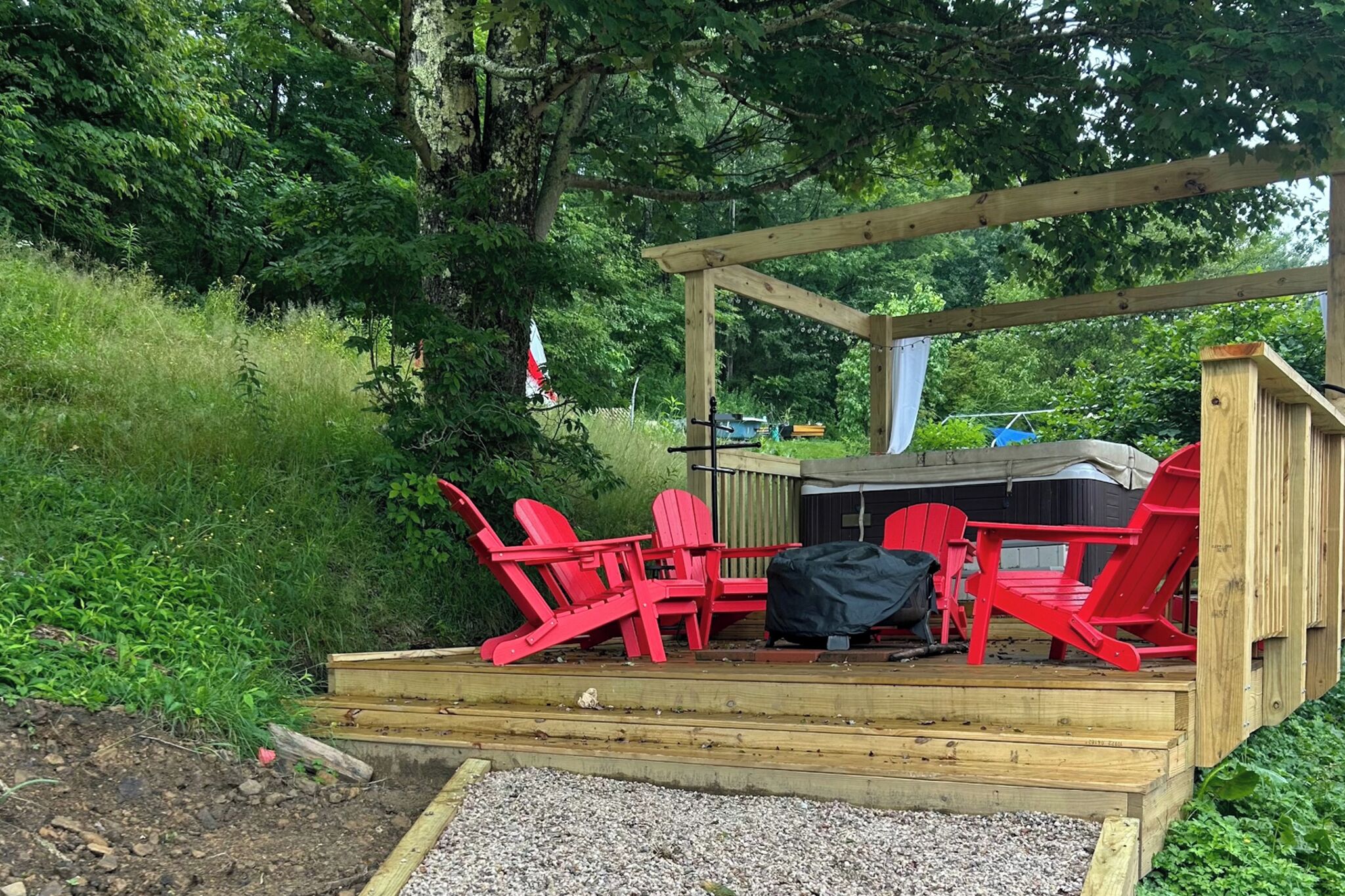 Een houten terras met buitenmeubilair, zoals stoelen en een tafel, met een achtergrond van bomen en groen.