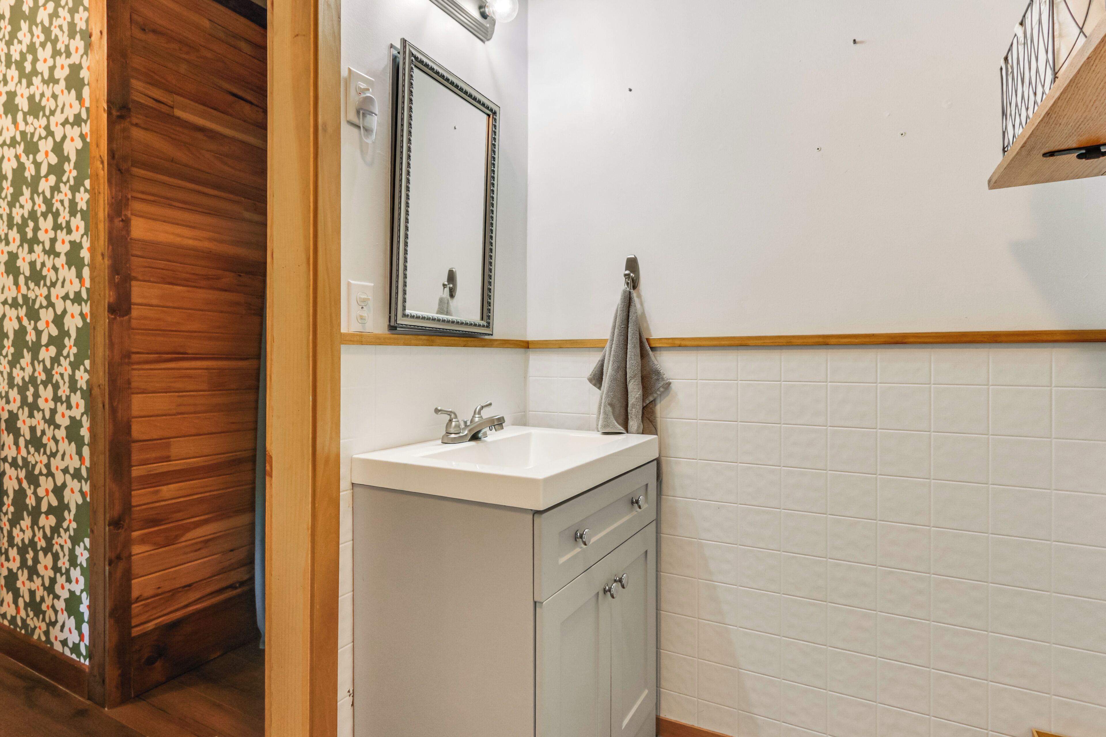 Ein Badezimmer mit Holztür, Waschbecken mit Spiegel darüber und einem Handtuch an der Wand.