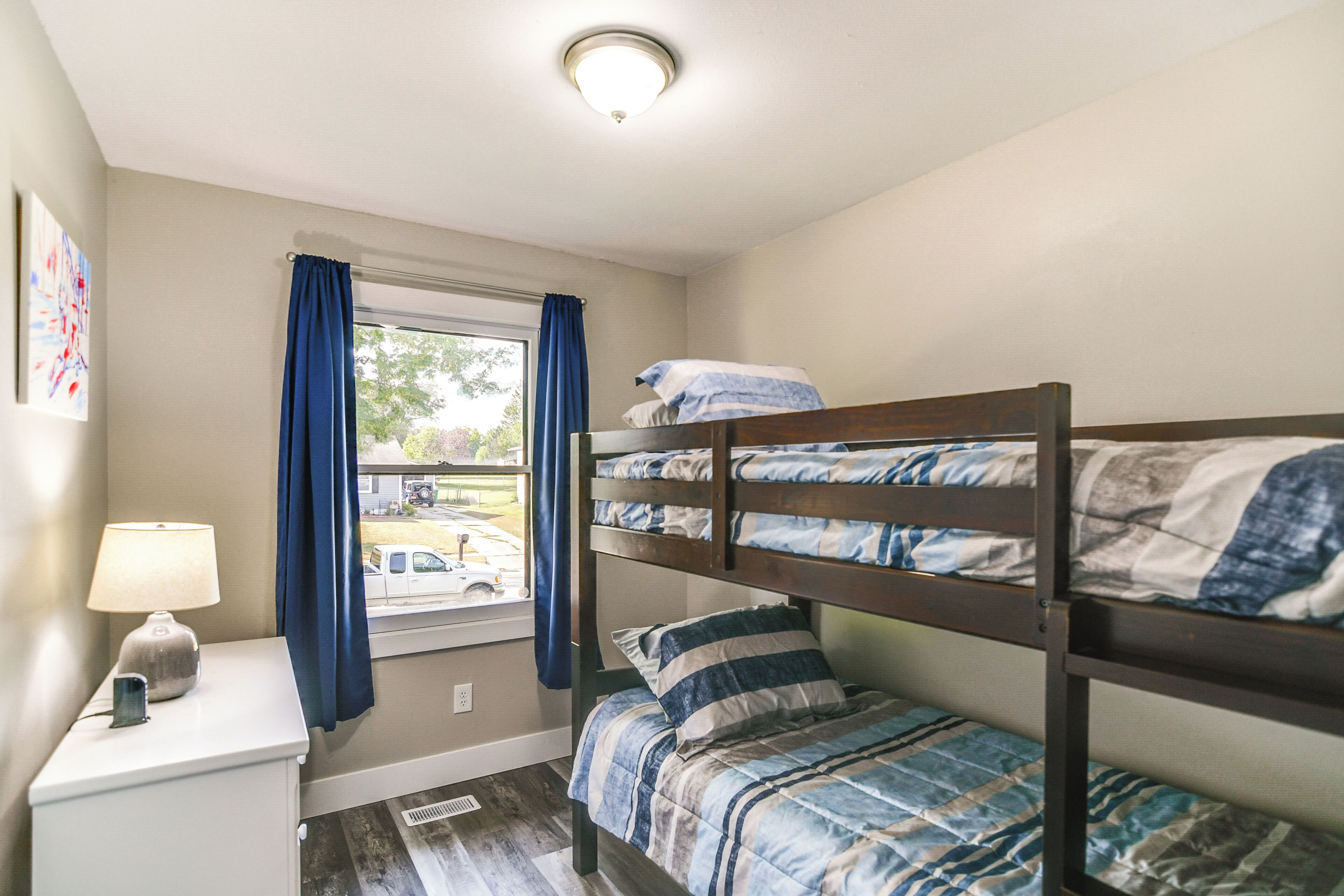 A bunk bed room with a window, a nightstand, and a lamp.
