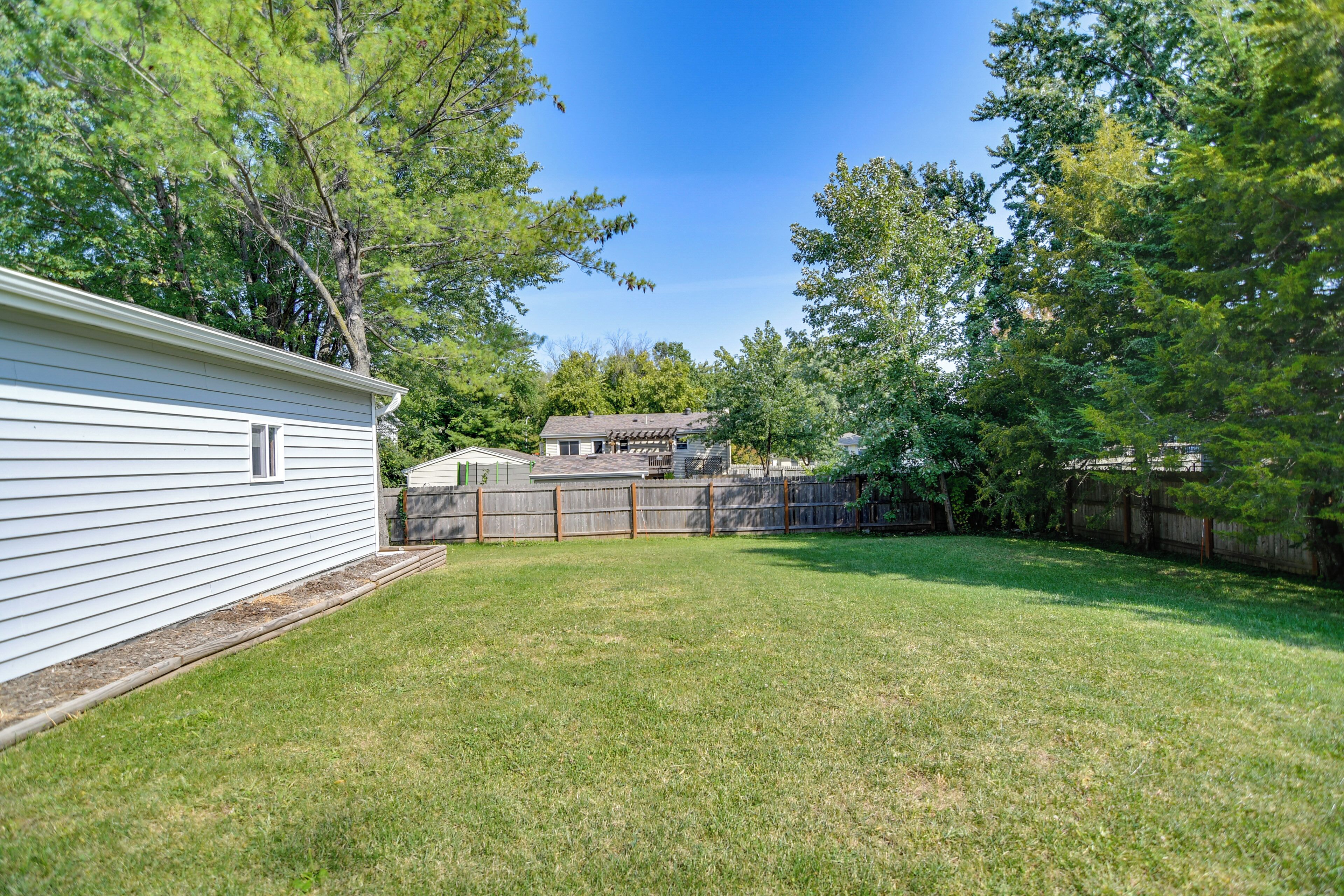 A backyard with a white house, a wooden fence, and trees.