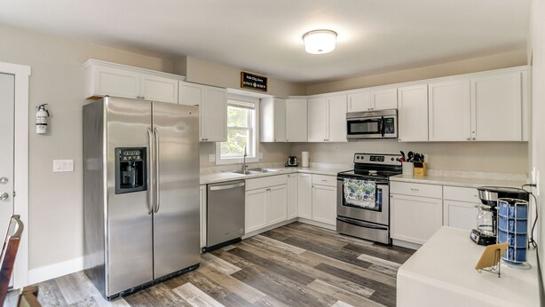 Una cocina moderna con armarios blancos, electrodomésticos de acero inoxidable y piso de madera con diseño espiga.