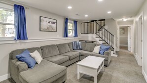 Una sala de estar con un sofá seccional gris, una mesa de centro blanca y cortinas azules en las ventanas.
