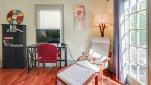 A living room with a TV, a red chair, a white armchair, a bookshelf, and a window with curtains.