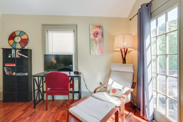 A living room with a TV, a red chair, a white armchair, a bookshelf, and a window with curtains. - Historic Home on French Creek - 2 Blocks to Dtwn (Franklin)