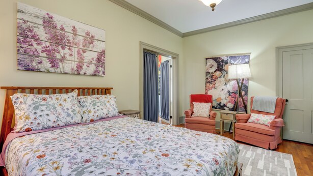 A bedroom with a large bed, a chair, a desk, and a door.