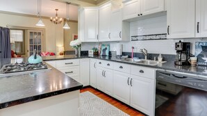 A modern kitchen with white cabinets, a black countertop, stainless steel appliances, and pendant lighting.